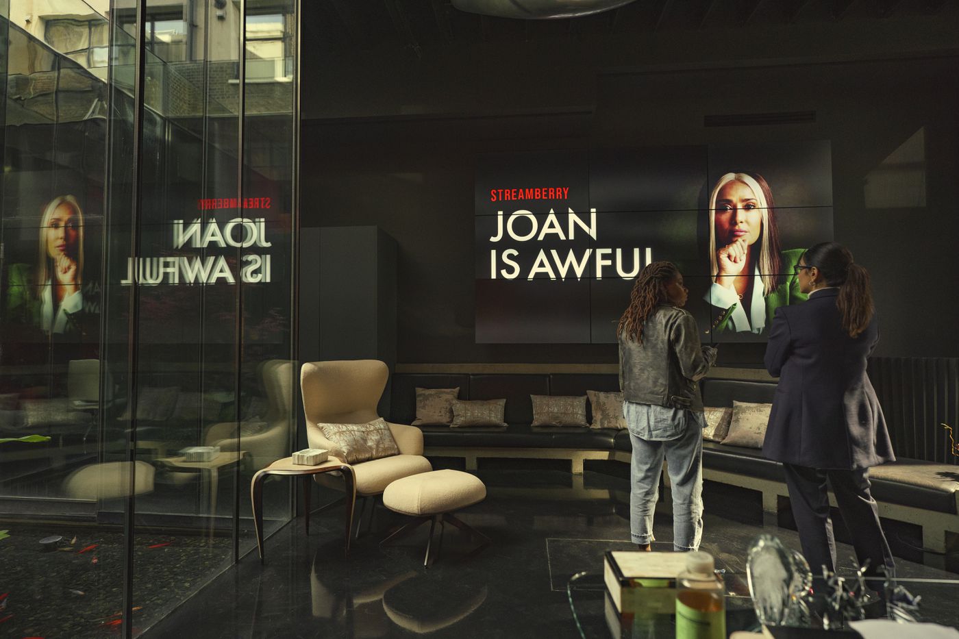 two executive women in a glass office setting looking at a poster for a streaming show